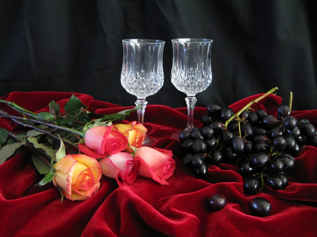 Wine glass on Silk bedsheet with roses and black grapes