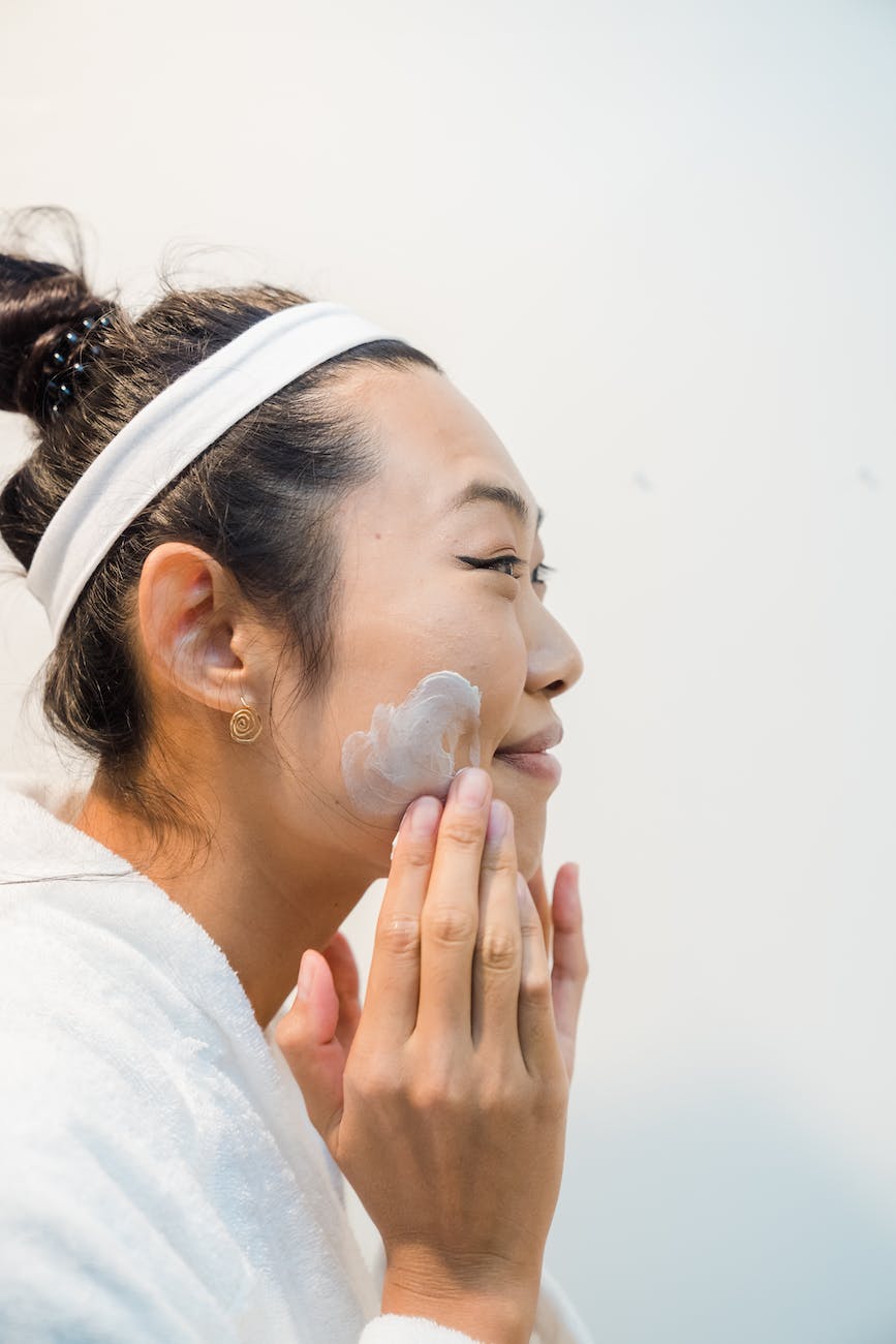 smiling woman applying facial cream on her face following her skin care routine